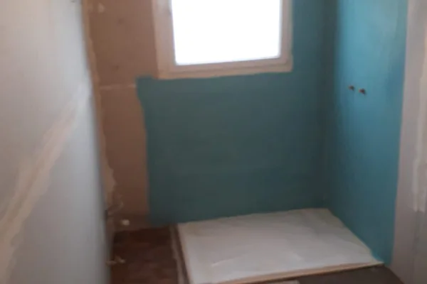 Salle de bains en rénovation : receveur de douche et cloison hydrofuge bleue sous la fenêtre